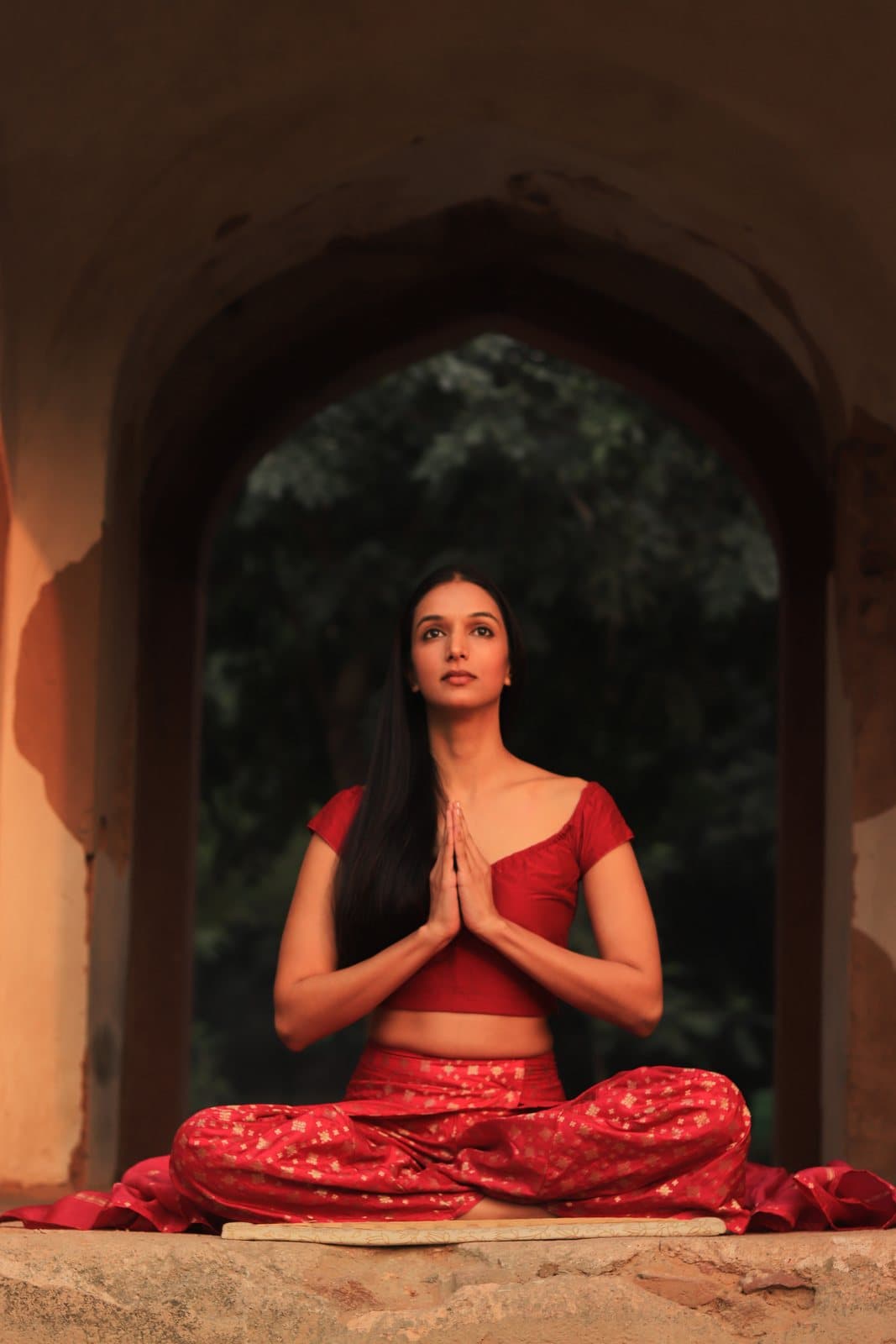Ira Trivedi seated in meditation beneath a sandstone arch